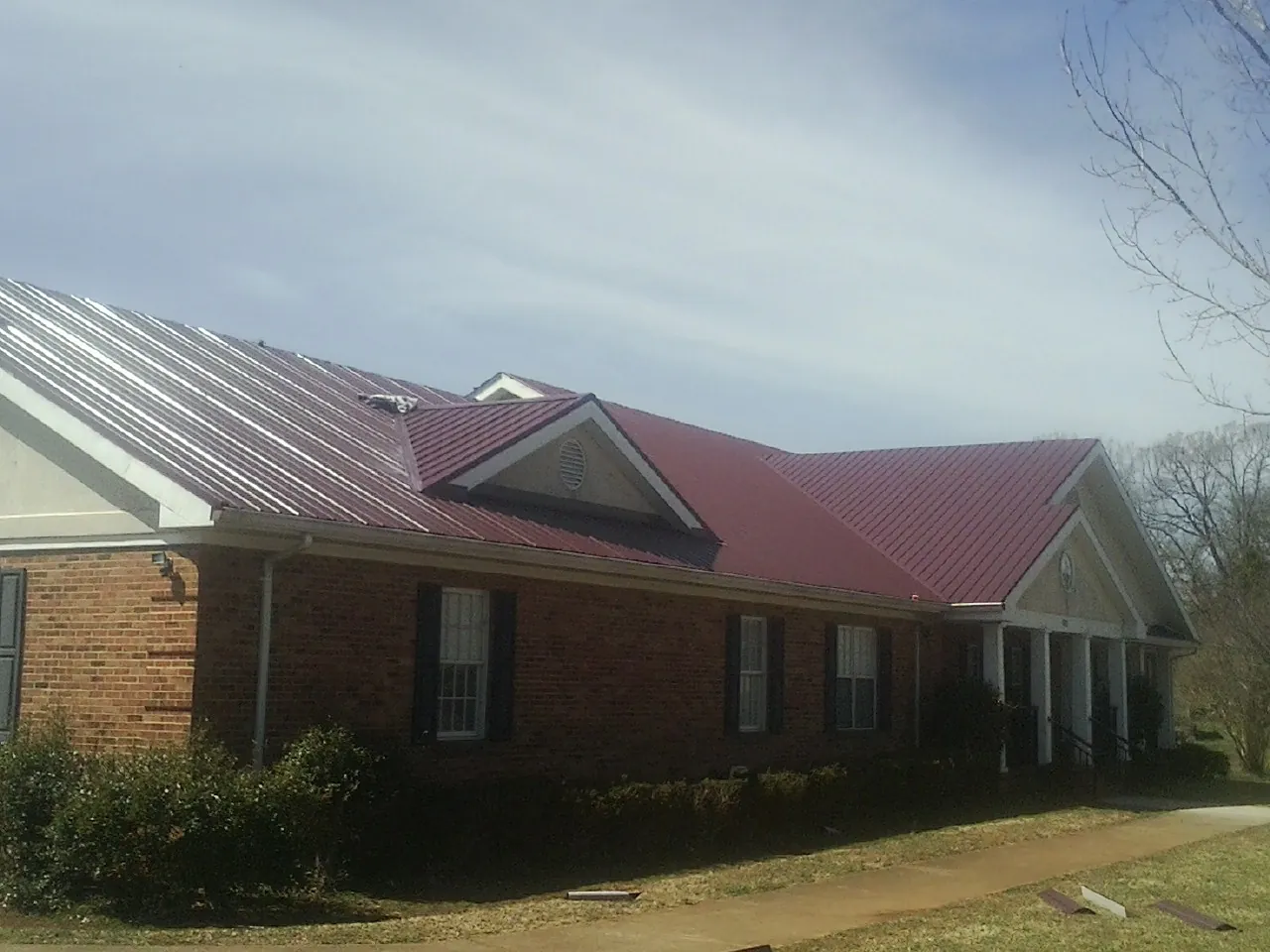Red metal roof with gabled entries on a long brick building, from a Hail Damage Roof Repair job in Middle Grove