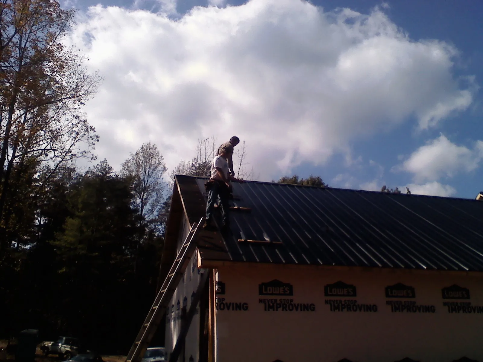 Roofer fastening dark metal panels high against a cloudy sky, from a Roof Inspection job in Middle Grove