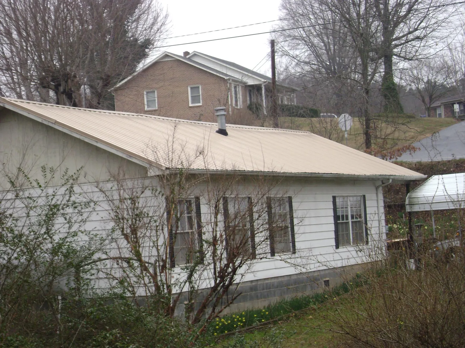 Tan metal roof on a white sided house set into a hillside — Commercial Roofing by Roofing Brothers in Middle Grove