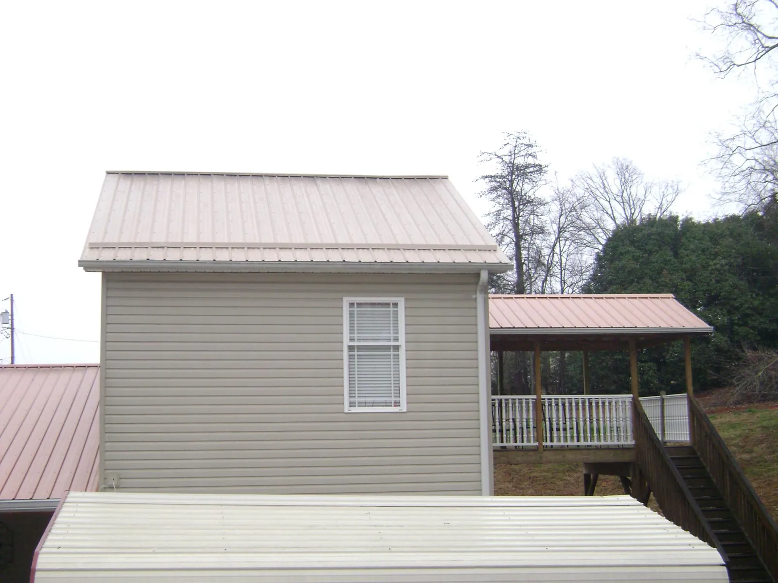 Tan metal roofs on a two story addition and attached porch, from a Roof Replacement job in Middle Grove